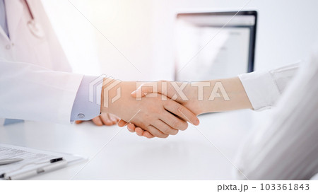 Doctor and patient shaking hands while sitting opposite of each other at the table in clinic, just hands close up. Medicine concept 103361843