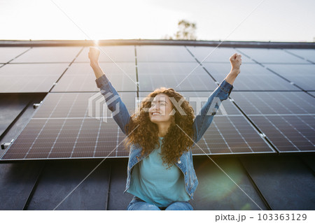 Portrait of young excited woman on roof with solar panels. 103363129