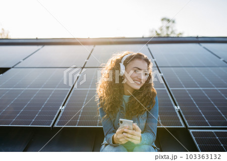 Portrait of young excited woman on roof with solar panels, listening music. 103363132