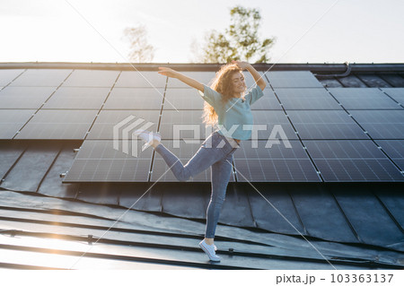 Portrait of young excited woman on roof with solar panels. 103363137