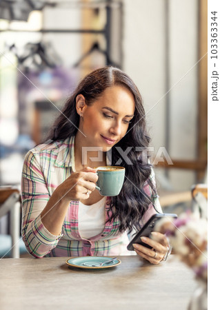 Portrait of beautiful woman using her smarphone in cafe, he reads received messages and follows social networks. 103363344