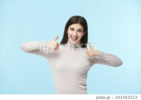 portrait of a beautiful young caucasian woman with two thumbs up, looking at camera smiling 103363523