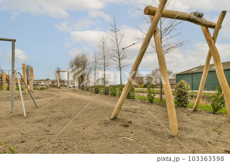 an outdoor play area with swings and wooden poles in the fore - image is taken from below, it's blue sky 103363598