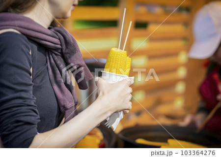 Cooked sweet corn on stick in hand of girl. Summer vegan dinner or appetizer, grilling 103364276