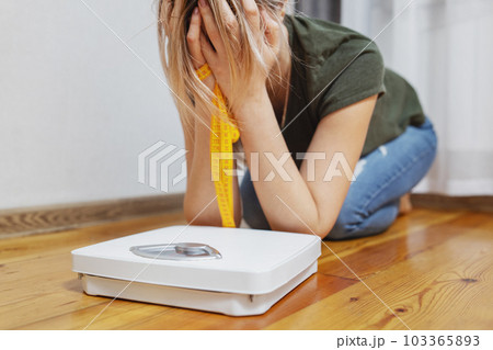 White scale and depression, upset and sad woman with measuring tape on floor 103365893