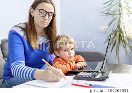 Business woman is working at home on a laptop with her baby.  103365931