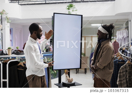Mall employee advertising shoes brand to buyer, showcasing brand new collection on empty digital whiteboard mock up. Store assistant showing stiletto to customer on interactive display 103367315