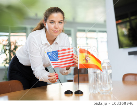 Positive young woman putting little flag of the USA on table next to the flag of Spain Positive young woman putting little flag of the USA on table next to the flag of Spain 103369946