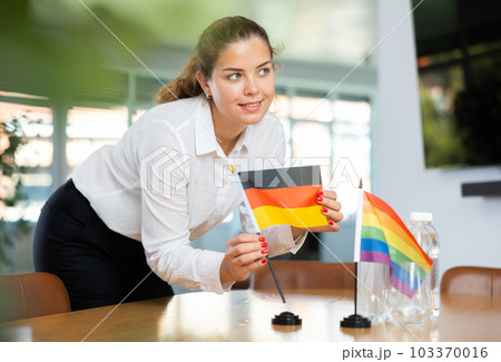 Unrecognizable girl sets up miniature LGBT and German flags before international talks 103370016
