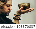 A man with closed eyes listens to the singing bowls. A man holds singing bowls in front of him. The rosary on hand.  Music of Tibetan singing bowls. Himalayan bowls. 103370837