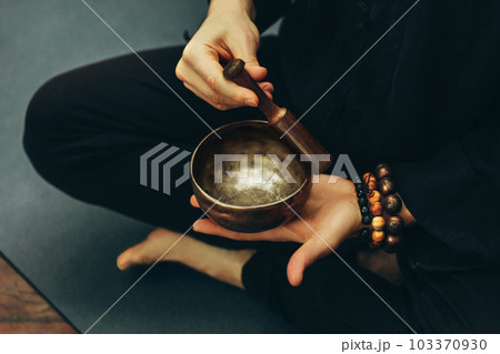 top view of a man sitting in a lotus position with a rosary on his hand playing on singing bowls. Relaxation and meditation. Alternative medicine. Tibetan and Himalayan singing bowls. Making sound. 103370930