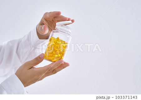 A hand holds a jar of OMEGA 3 capsules. 103371143