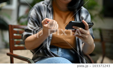 A woman showing clenched fist while watching something on her smartphone outdoors. A woman showing clenched fist while watching something on her smartphone outdoors. 103371243