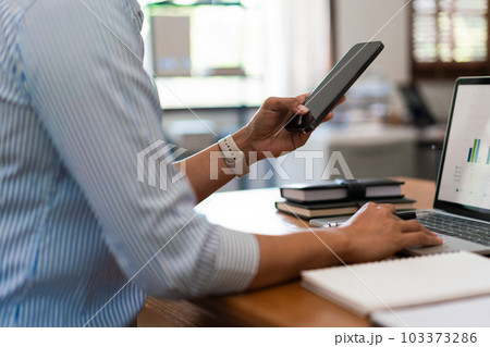 Close up of businesswoman searching business data on smartphone while working on laptop in office 103373286
