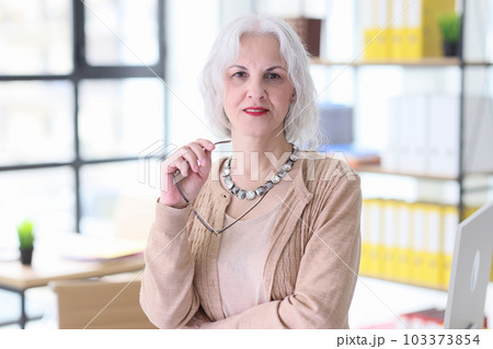 Senior grey-haired woman stands in office looking at camera Senior grey-haired woman stands in office looking at camera 103373854