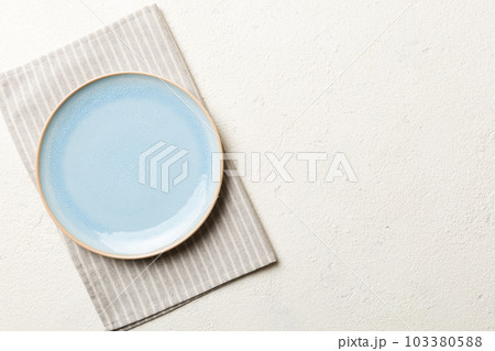 Top view on colored background empty round blue plate on tablecloth for food. Empty dish on napkin with space for your design Top view on colored background empty round blue plate on tablecloth for food. Empty dish on napkin with space for your design 103380588