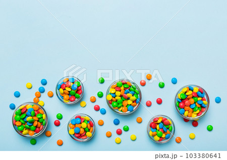 different colored round candy in bowl and jars. Top view of large variety sweets and candies with copy space different colored round candy in bowl and jars. Top view of large variety sweets and candies with copy space 103380641