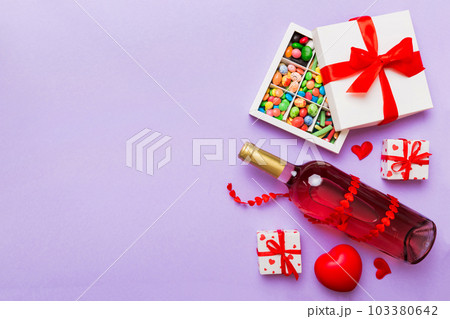 Bottle of red wine on colored background for Valentine Day with gift and chocolate. Heart shaped with gift box of chocolates top view with copy space 103380642