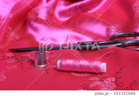Spool of Pink Thread and Thimble on Vintage Pink Satin Fabric Spool of Pink Thread and Thimble on Vintage Pink Satin Fabric 103381666