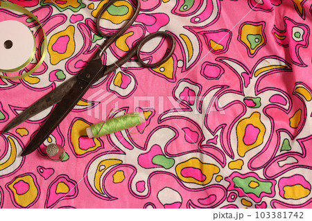 Spool of Green Thread, Thimble and Needle on Retro Pink and Green Fabric Spool of Green Thread, Thimble and Needle on Retro Pink and Green Fabric 103381742
