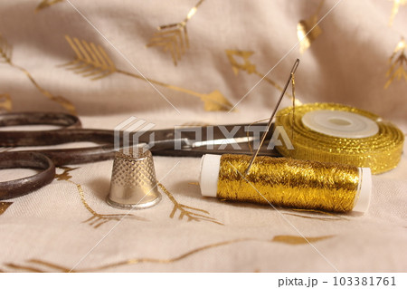 Spool of Gold Thread and Scissors With Thimble on Metallic Fabric Spool of Gold Thread and Scissors With Thimble on Metallic Fabric 103381761