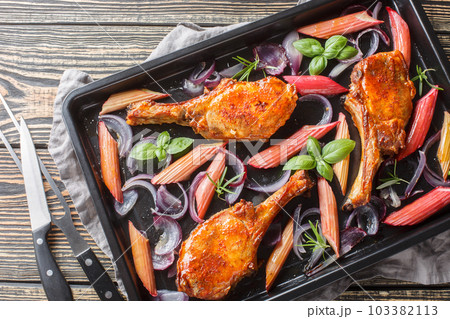 Homemade baked pork chops with red onions, herbs and rhubarb close-up in a baking sheet. Horizontal top view 103382113