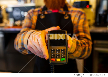 Professional barista young redhaired ginger bearded man in black apron working in coffee shop 103382323