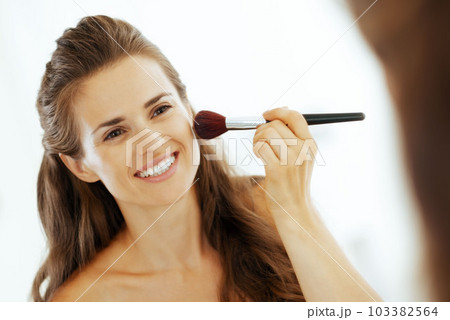 Happy young woman applying makeup in bathroom Happy young woman applying makeup in bathroom 103382564