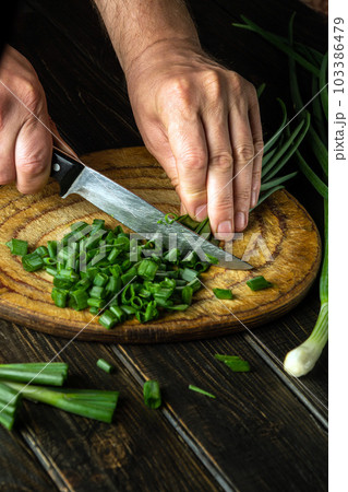 Chef cutting green onion on a cutting board with a knife for preparing a vegetarian dish. Peasant food 103386479