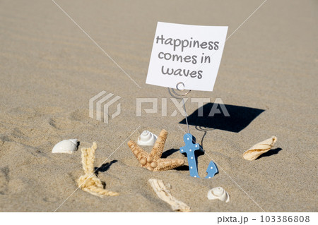 HAPPINESS COMES IN WAVES text on paper greeting card in anchor paper holder and starfish seashell summer vacation decor. Sandy beach sun coast. Holiday concept postcard. Getting away Travel HAPPINESS COMES IN WAVES text on paper greeting card in anchor paper holder and starfish seashell summer vacation decor. Sandy beach sun coast. Holiday concept postcard. Getting away Travel 103386808