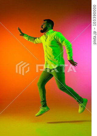Full-length portrait of handsome bearded man in casual clothes jumping against gradient studio background in neon light Full-length portrait of handsome bearded man in casual clothes jumping against gradient studio background in neon light 103390000