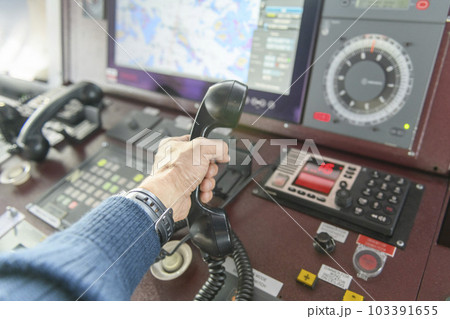 Navigational control panel and VHF radio with hand. Radio communication at sea. Working on the ship's bridge. Navigational control panel and VHF radio with hand. Radio communication at sea. Working on the ship's bridge. 103391655