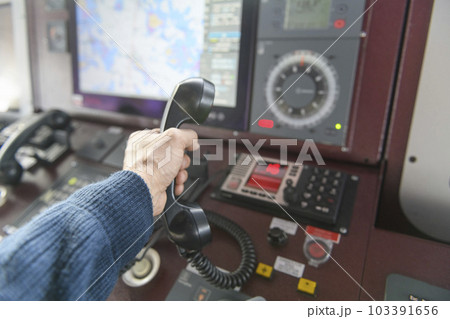 Navigational control panel and VHF radio with hand. Radio communication at sea. Working on the ship's bridge. Navigational control panel and VHF radio with hand. Radio communication at sea. Working on the ship's bridge. 103391656