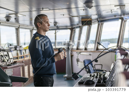 Deck officer with binoculars on navigational bridge. Seaman on board of vessel. Commercial shipping. Cargo ship. Deck officer with binoculars on navigational bridge. Seaman on board of vessel. Commercial shipping. Cargo ship. 103391779