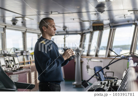 Deck officer with binoculars on navigational bridge. Seaman on board of vessel. Commercial shipping. Cargo ship. Deck officer with binoculars on navigational bridge. Seaman on board of vessel. Commercial shipping. Cargo ship. 103391781