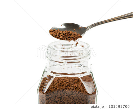 Granulated instant coffee is poured from a spoon into a glass jar of coffee. 103393706