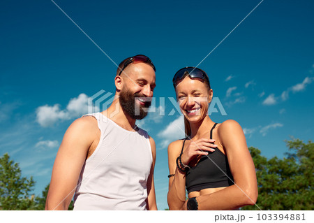 Althetes man and woman 25-35 years old, posing for the camera, smiling, running against the backdrop of a stadium with a blue sky, cardio workout, weight loss, keep yourself in good shape 103394881