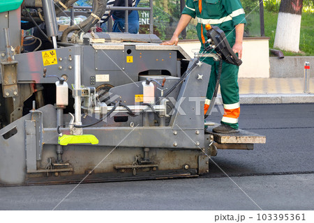 A fragment of the work of an industrial asphalt paver, an engineer stands on the footboard and controls the process. 103395361