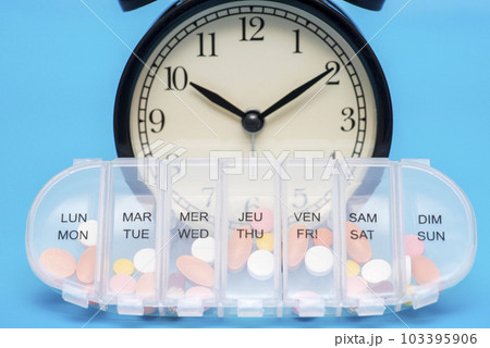 Black alarm clock and 7 day plastic pill organizer on blue background. Black alarm clock and 7 day plastic pill organizer on blue background. 103395906