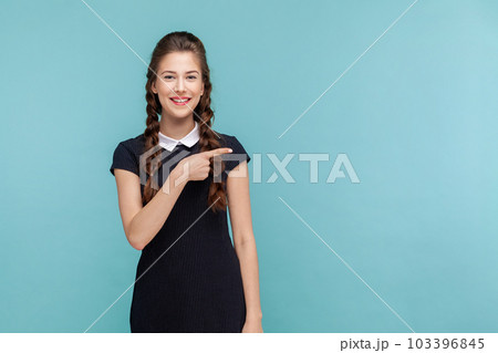 Your advertising here. Portrait of woman points away on copy space, suggests follow this direction or click on link, wearing black dress. woman Indoor studio shot isolated on blue background. Your advertising here. Portrait of woman points away on copy space, suggests follow this direction or click on link, wearing black dress. woman Indoor studio shot isolated on blue background. 103396845