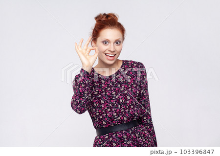 Portrait of delighted joyful cheerful young adult redhead woman wearing dress showing ok sign, looking at camera with toothy smile. Indoor studio shot isolated on gray background. Portrait of delighted joyful cheerful young adult redhead woman wearing dress showing ok sign, looking at camera with toothy smile. Indoor studio shot isolated on gray background. 103396847