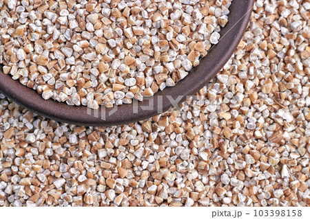 Crushed grain of wheat for making porridge close up against the background of scattered grains of wheat Crushed grain of wheat for making porridge close up against the background of scattered grains of wheat 103398158