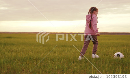 child girl runs across green field sunset kicking ball. children playing soccer ball sunset. football fan. lawn field. summer game evening rays sun. child run ball. little child kid girl daughter run child girl runs across green field sunset kicking ball. children playing soccer ball sunset. football fan. lawn field. summer game evening rays sun. child run ball. little child kid girl daughter run 103398198