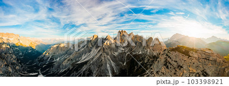Mountain landscape at sunrise. Rising sun rays illuminate stony treeless slopes of Three Peaks of Lavaredo under clear sky aerial view in back lit 103398921