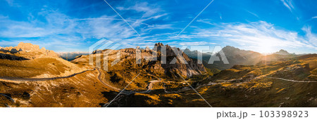 High stone columns of mountain massif of Tre Cime di Lavaredo at sunset. Battlement-like peaks under blue sky with white clouds aerial view 103398923