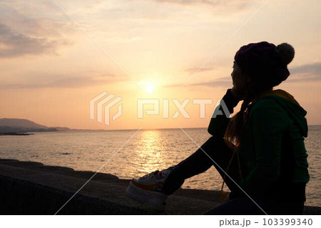 夕日の光が海面に反射する防波堤で佇む女性のシルエットとマジックアワーの風景 103399340