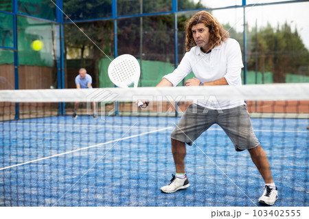 Portrait of middle-aged Latin male in sportswear enjoying popular sport padel game on tennis court outside Portrait of middle-aged Latin male in sportswear enjoying popular sport padel game on tennis court outside 103402555