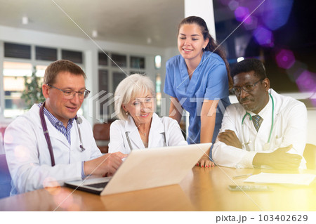 Doctor with colleagues sitting at table, reading new of law on laptop and discussing information 103402629