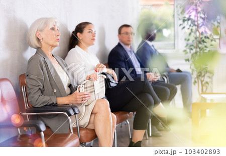 Serious-minded mature female candidate siting on chair and waiting for job interview in hallway 103402893