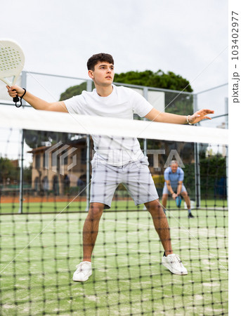 Young focused guy playing paddle tennis outdoors 103402977
